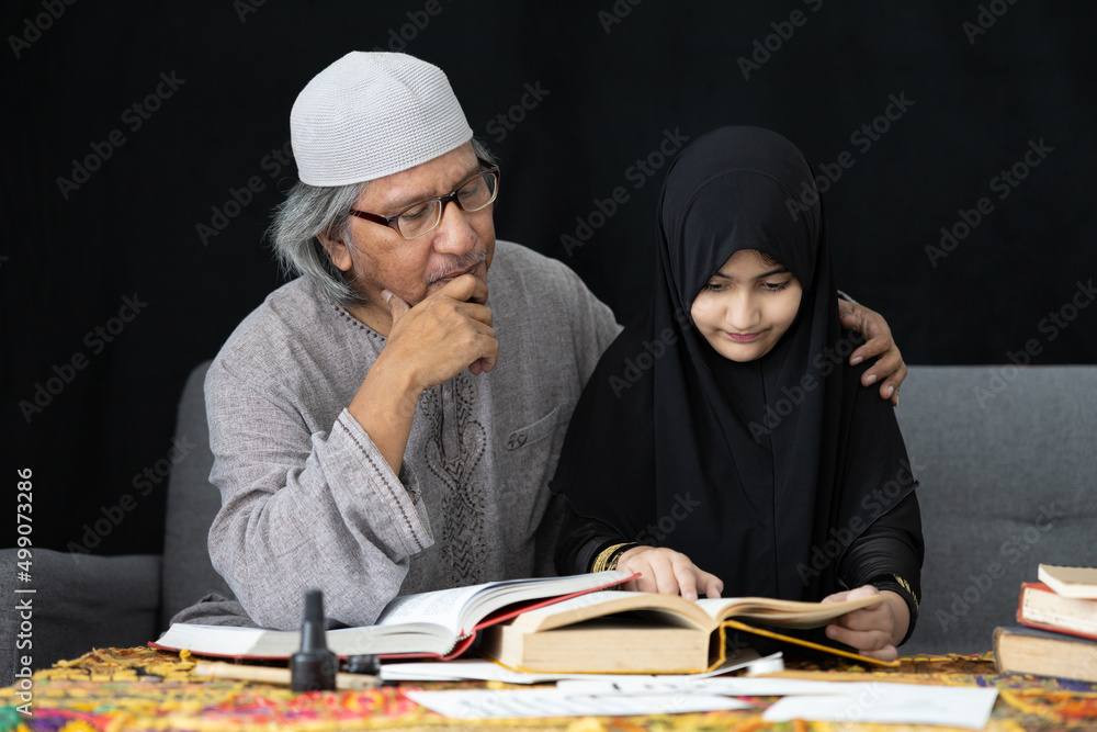 muslim father teaching his daughter about practicing reading textbook on black background muslim father teaching his daughter about practicing reading textbook on black background