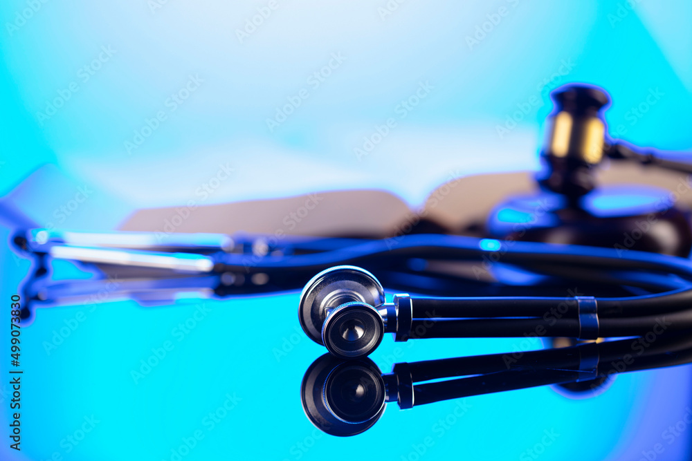 Medical law concept. Gavel, legal code and stethoscope on the glass table. Blue light. Medical law concept. Gavel, legal code and stethoscope on the glass table. Blue light.