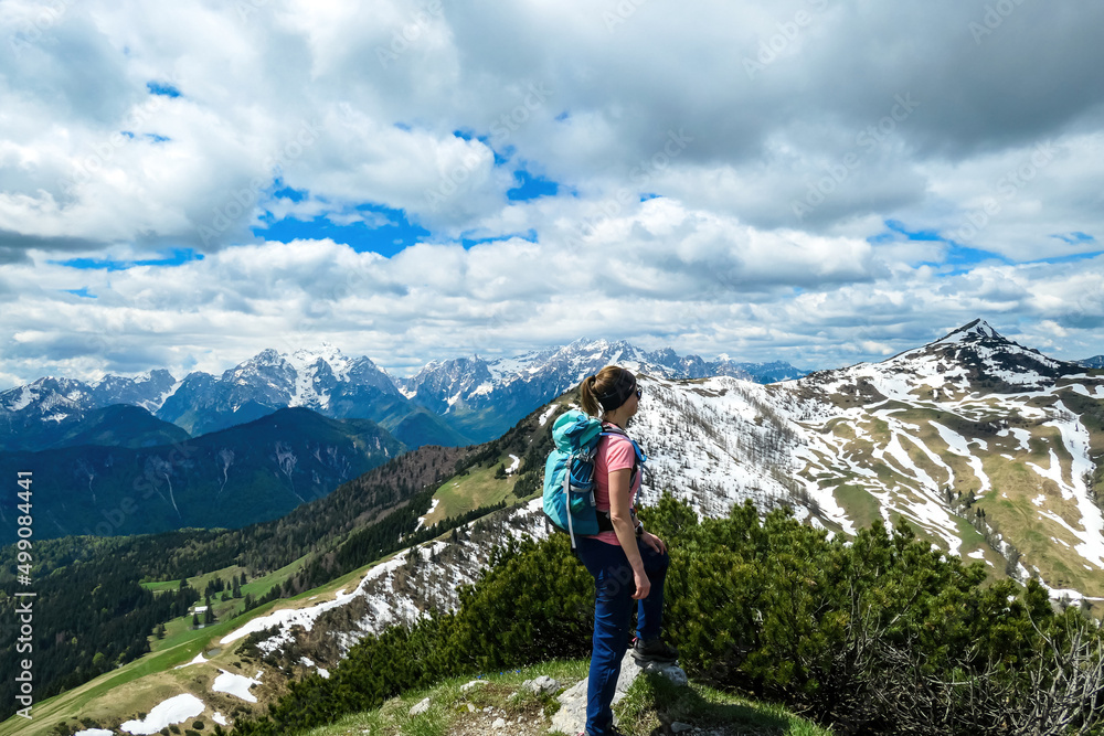 Hiker woman with backpack at summit of Hahnkogel (Klek) with scenic view on mountain peaks in Karawanks and Julian Alps, Carinthia, Austria. Border with Slovenia. Triglav National Park. Goal seeking