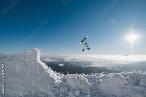 Snowboarder making high flip big air jump in clear blue sunny sky above mountains
