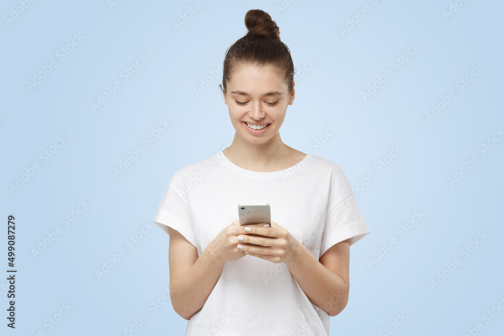 Modern young woman looking at smartphone, smiling openly while holding it Modern young woman looking at smartphone, smiling openly while holding it