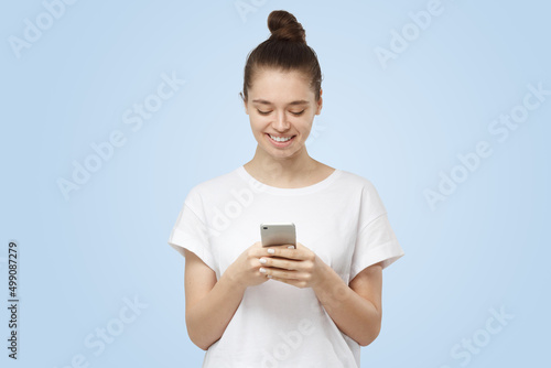 Modern young woman looking at smartphone, smiling openly while holding it