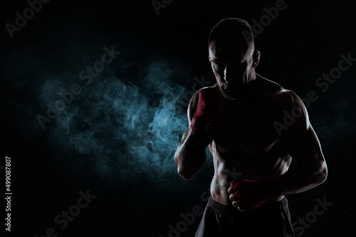 Kickboxer in red bandages poses against a background of smoke. The concept of mixed martial arts.