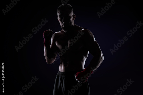 Kickboxer in red bandages posing on a blue background. The concept of mixed martial arts. © andy_gin