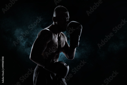 Kickboxer in black gloves posing on a background of smoke. The concept of mixed martial arts.