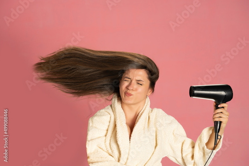 Murais de parede Funny woman drying her long hair with electric fan on a pink background