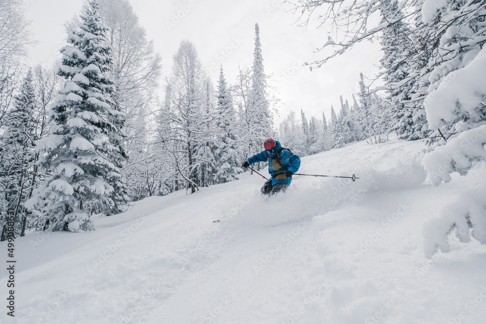 Skier moving in snow powder in forest on a steep slope of  ski resort. Freeride, winter sports outdoor