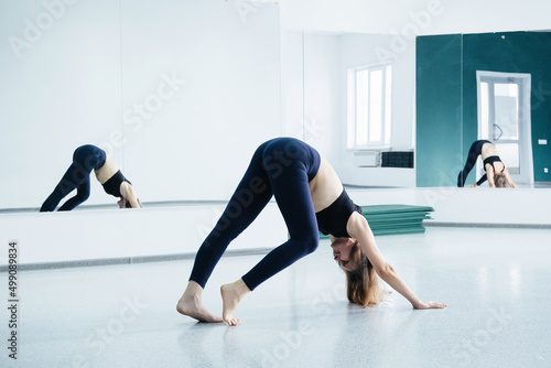 Attractive female middle age 50 years old doing yoga exercise near big mirror in empty yoga studio