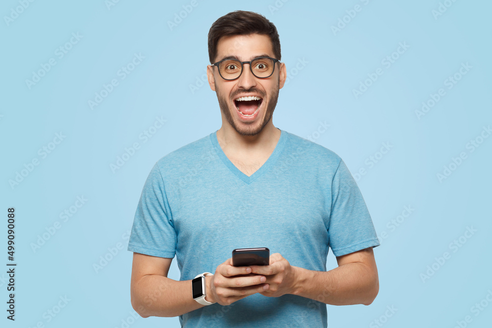 Young handsome man holding phone in hands, looking at camera with excited WOW face Young handsome man holding phone in hands, looking at camera with excited WOW face