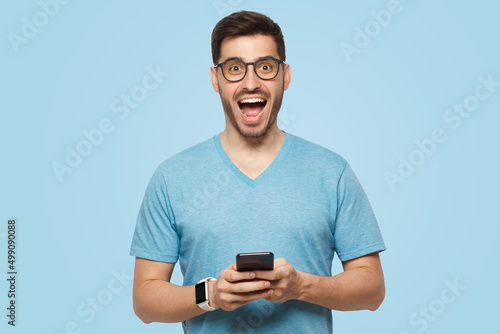 Young handsome man holding phone in hands, looking at camera with excited WOW face © Damir Khabirov