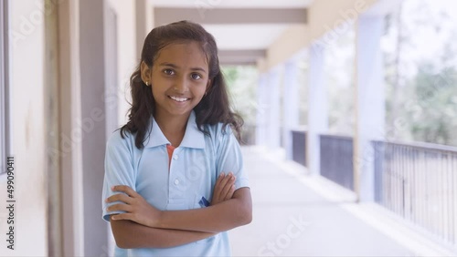 hand held shot of Smiling girl kid standing with crossed arms by looking at camera at school corridor - concept of education, back to school and development photo