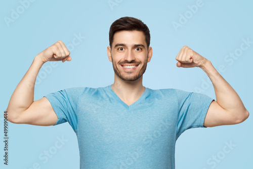 Strong and sporty athletic man in casual blue t-shirt, showing two biceps after training in gym