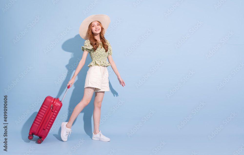 Full length image of young Asian girl with suitcase on blue background, travel concept Full length image of young Asian girl with suitcase on blue background, travel concept