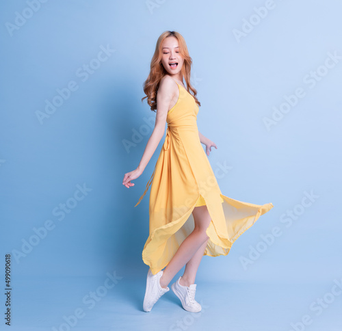 Obraz na plátne Full length image of young Asian woman wearing yellow dress on blue background