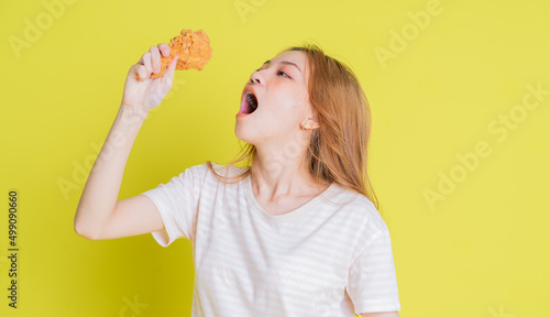 Image of young Asian girl eating chicken fried on yellow background