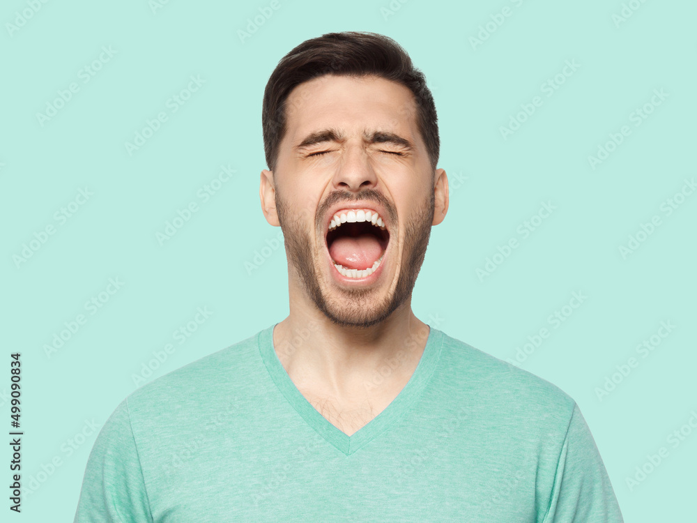 Young man in t-shirt screaming loudly with closed eyes, feeling strong anger and despair Young man in t-shirt screaming loudly with closed eyes, feeling strong anger and despair