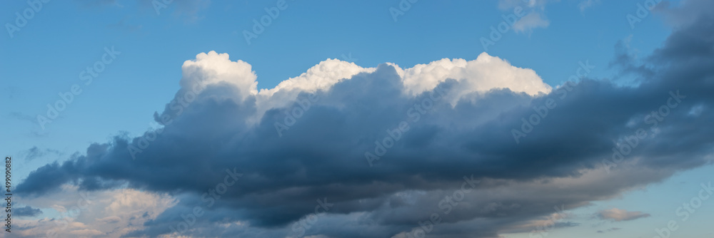 Banner with panoramic view over deep blue rainy sky with illuminated clouds as a background.