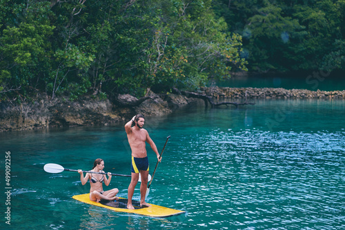 Summer holidays vacation travel. SUP Stand up paddle board. Young woman and man sailing together on beautiful calm lagoon. photo