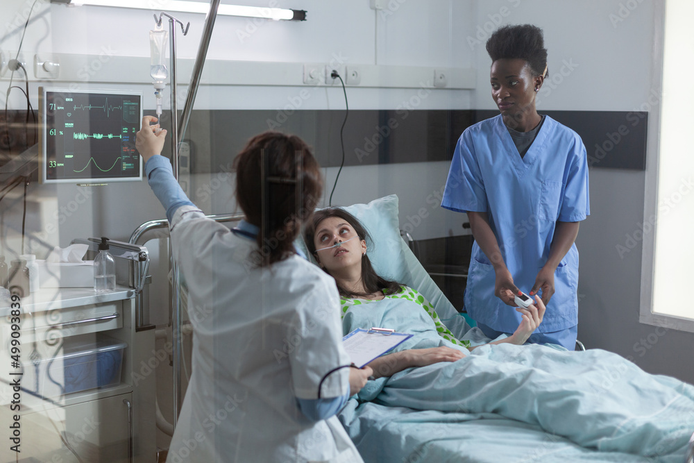 Doctor setting up central line catether with iv drip medication to patient while nurse is putting pulse oximeter on finger. Woman in hospital bed looking at doctor giving her intravenous antibiotics. Doctor setting up central line catether with iv drip medication to patient while nurse is putting pulse oximeter on finger. Woman in hospital bed looking at doctor giving her intravenous antibiotics.