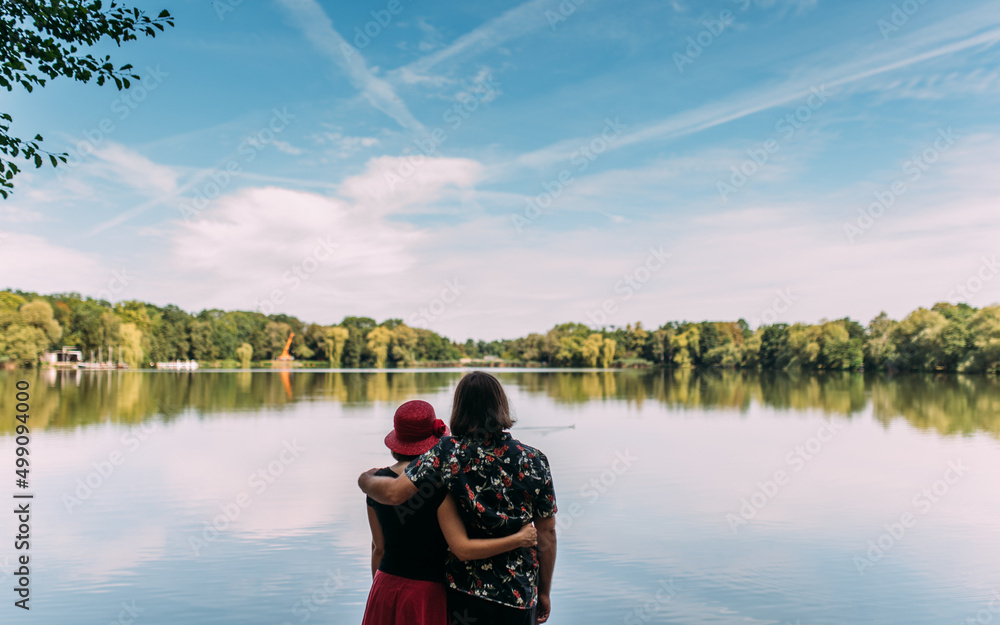 Obraz premium verliebtes Paar stehend von hinten an einem See mit Blick auf das Wasser mit Blick in die friedliche Zukunft in Familie
