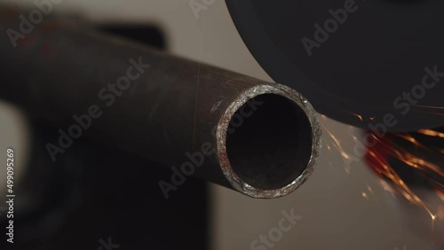 Closeup of metal pipe that is being sawed by an angle grinder with cutting disc, sparks everywhere. Artisan sawing metal pipe using angle grinder