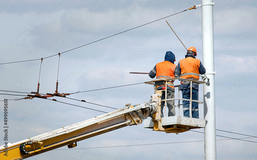 Workers in aerial platform paint street light pole at height. Man in cradle painting lamppost with paint brush. Cherry picker with worker at height, risky job. Paint and renovate street lightning pole Workers in aerial platform paint street light pole at height. Man in cradle painting lamppost with paint brush. Cherry picker with worker at height, risky job. Paint and renovate street lightning pole