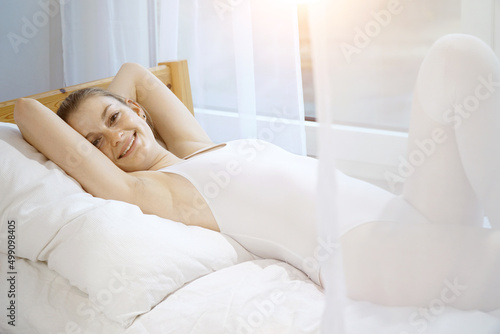 Beautiful pretty girl wears white body suit as underwear and lies relaxed on bed