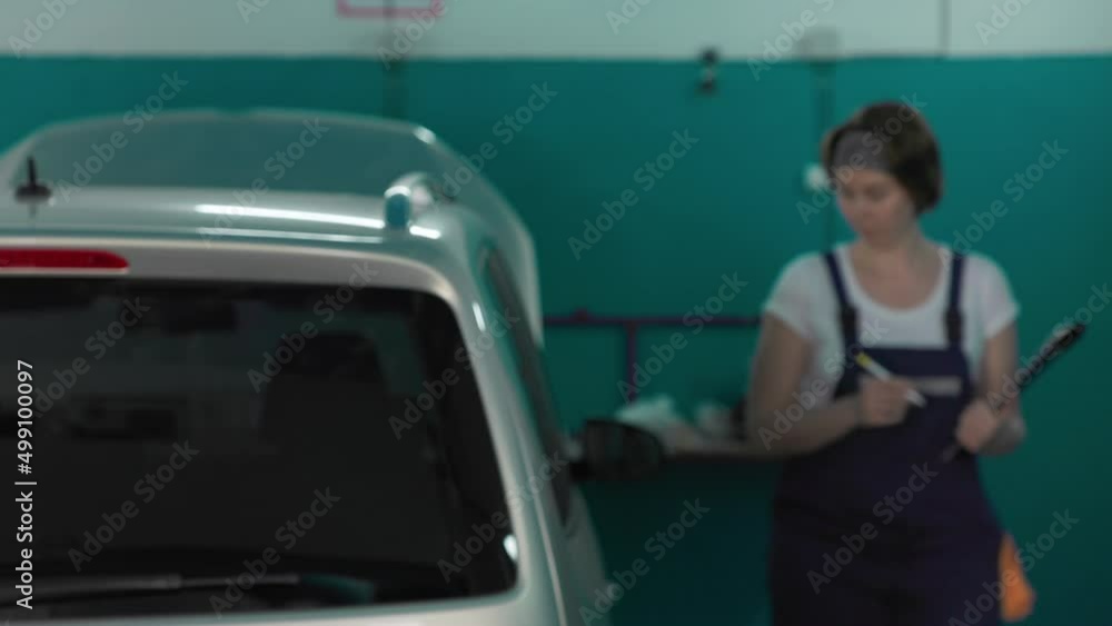 A young female mechanic inspects the car and signs documents to repair the vehicle. The concept of women's equality and work in an auto repair shop. A young female mechanic inspects the car and signs documents to repair the vehicle. The concept of women's equality and work in an auto repair shop.
