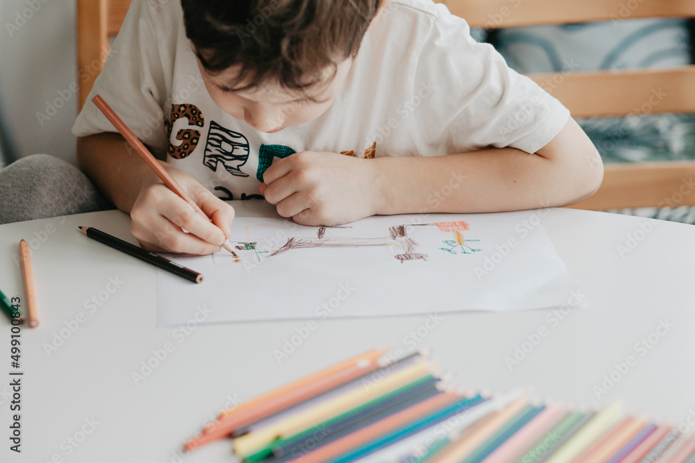 The boy draws with pencils at the kitchen The boy draws with pencils at the kitchen