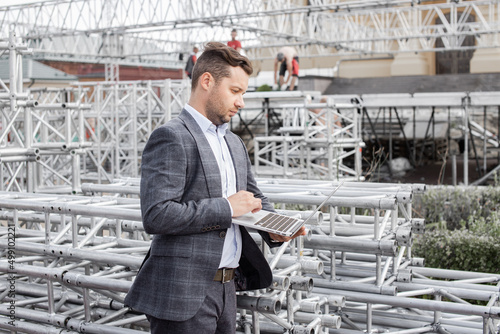 Installation of stage equipment and preparing for a live concert open air. Event manager portrait. Summer music city festival. Man work with laptop.