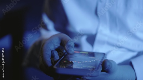 A close-up of a man's hand with a phone, the screen shows an online stock market chart showing bitcoin currencies. In blue light. In real time. Cryptocurrency. Investors