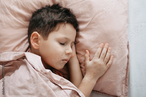 The boy sleeps in the bedroom, head on a pillow, under a blanket
