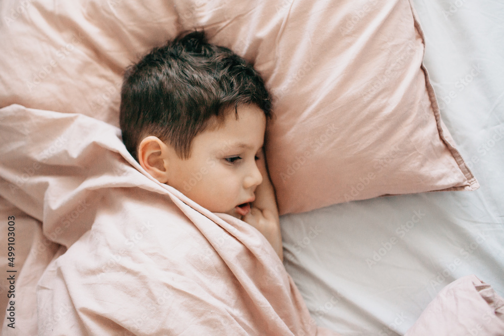 The boy sleeps in the bedroom, head on a pillow, under a blanket The boy sleeps in the bedroom, head on a pillow, under a blanket