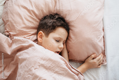 The boy sleeps in the bedroom, head on a pillow, under a blanket