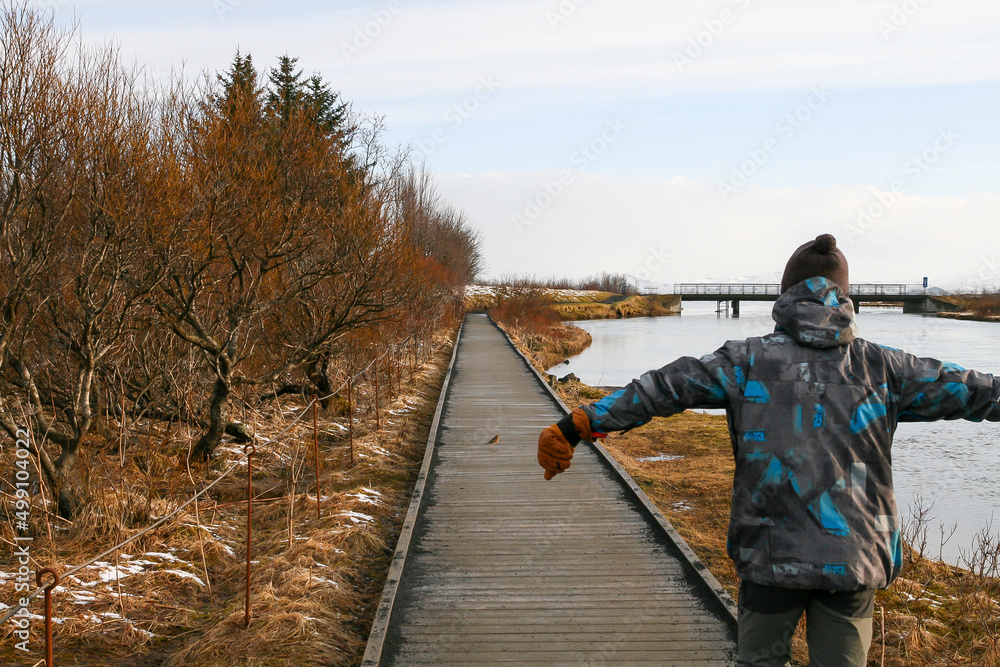 Man in a blue jacket walks with his arms outstretched on a boardwalk along a lake in autumn Man in a blue jacket walks with his arms outstretched on a boardwalk along a lake in autumn