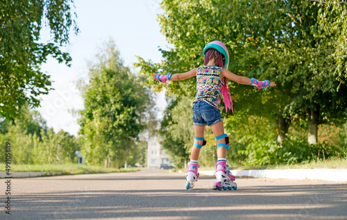 Wallpaper Mural Kid tries to keep his balance and not fall, for the first time standing on roller skates. view behind. A girl is learning to rollerblade. Active sports for summer recreation and outdoor entertainment Torontodigital.ca