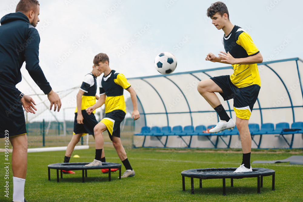Fototapeta premium Teenage boy in football training with personal coach. Soccer players improving agility soccer skills. Boy kicking soccer ball standing on fitness trampoline