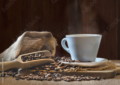 Steaming cup of coffee ready to drink. Coffee beans coming out of a cloth sack filling the cup. A wooden spoon filled with coffee beans.Copy space.
