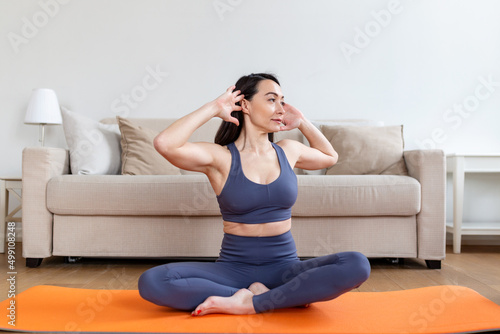 Asian attractive smiling woman practicing yoga, sitting in Half Lotus exercise, Ardha Padmasana pose, working out, wearing sportswear, meditation session, indoor full length, home interior photo
