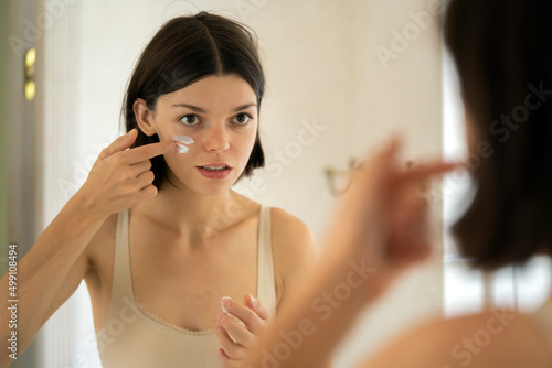 Girl applies cream on her face.