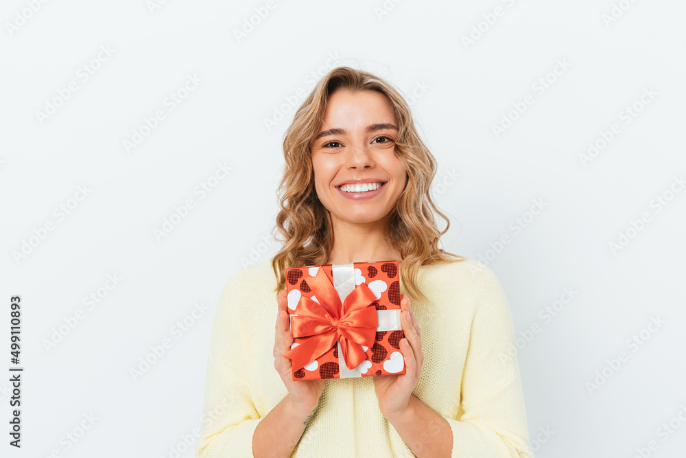 Happy young woman holding gift box smiles and looking at camera Happy young woman holding gift box smiles and looking at camera
