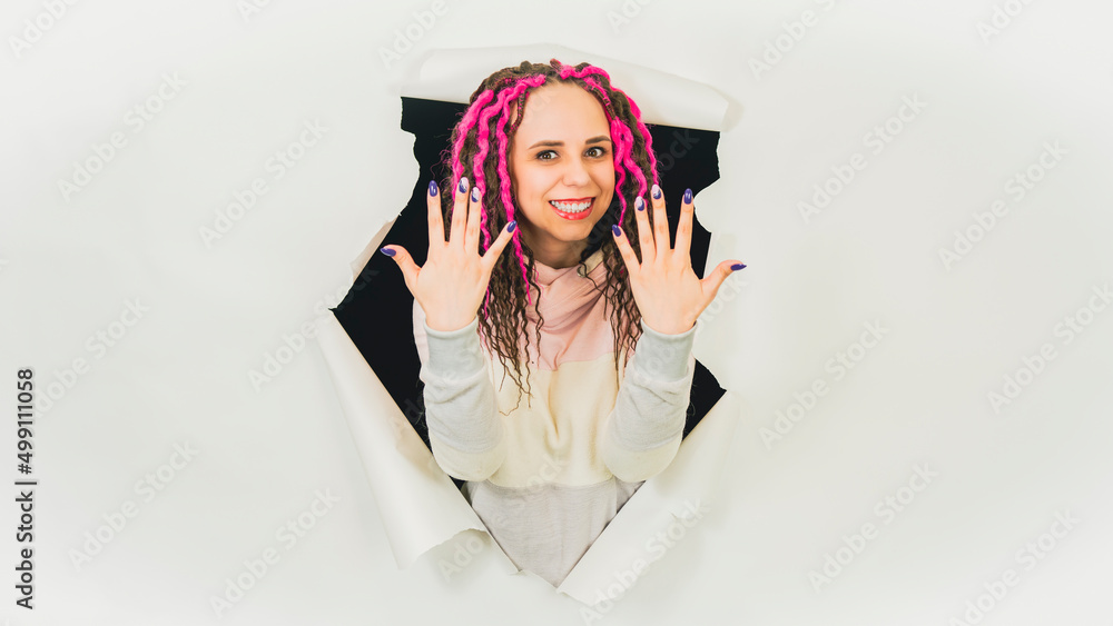 Naklejka premium Young woman showing manicure in hole of white background. Beautiful female with curly hair showing her hands with polish nails in studio.