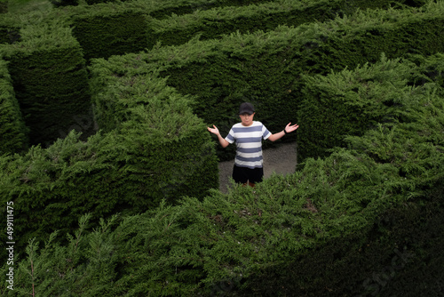 A boy in a hedge maze shrugging because he is lost