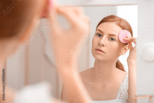 Young woman with makeup sponge near mirror at home photo