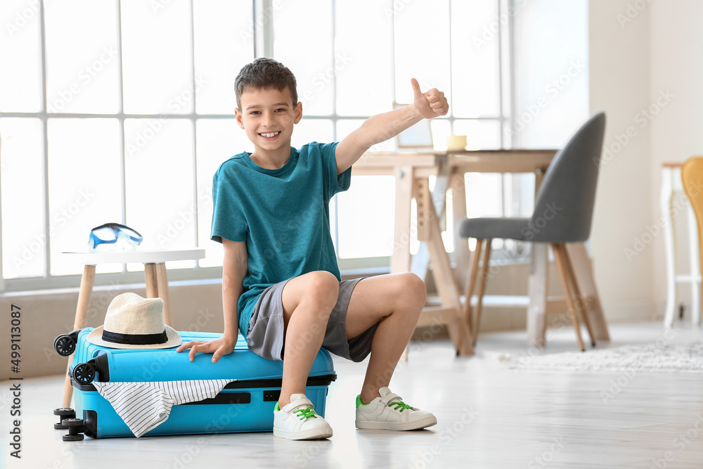 Obraz premium Happy little boy with packed suitcase at home