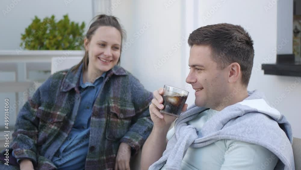 Causacian couple at the cafe terrace. Young man laughs sipping carbonated soft drink from the glass with ice and lemon slice. Causacian couple at the cafe terrace. Young man laughs sipping carbonated soft drink from the glass with ice and lemon slice.