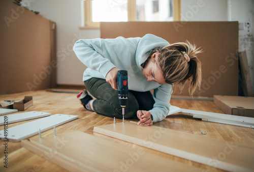 Woman assembling furniture at home with cordless screwdriver