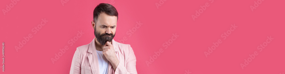 Fototapeta premium Handsome man with a beard in a pink jacket is thinking over an isolated red background.