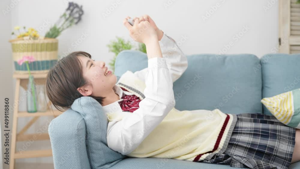 ソファーでスマートフォンを操作する女子高生 ソファーでスマートフォンを操作する女子高生