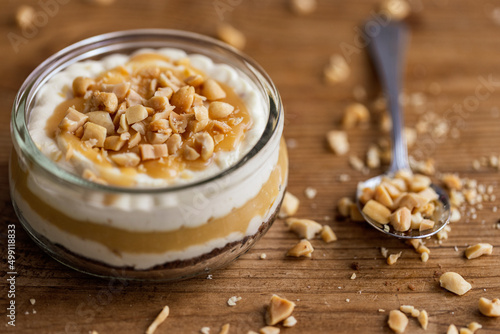 Snickers toffee cream peanut layered dessert in a glass jar on a wooden background photo